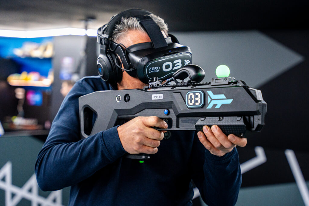 Muž s VR headsetem držící zbraň hraje hru Undead arena